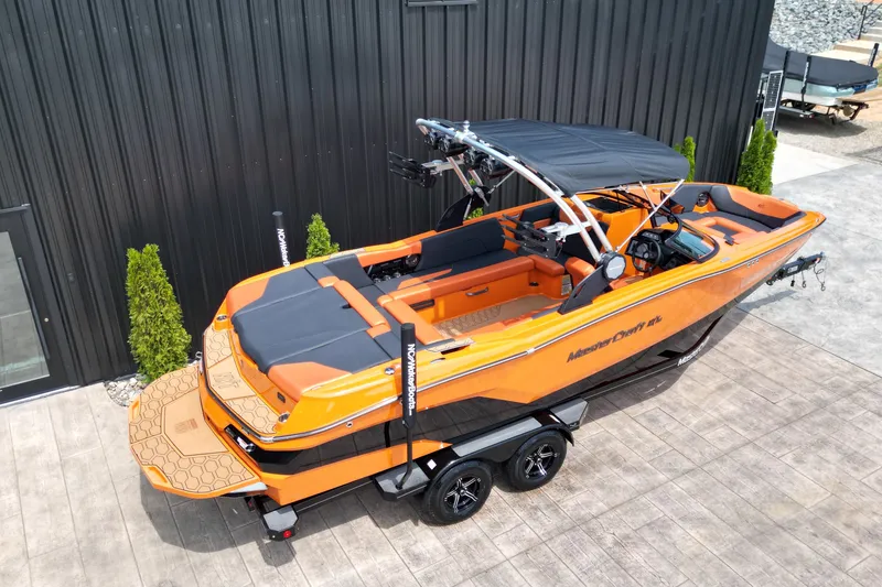 Slide: The Image of 2022 MasterCraft NXT24 boat in vibrant orange, parked on a trailer beside a modern building. - 3