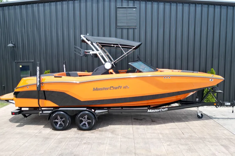 The Image of 2022 MasterCraft NXT24 boat in vibrant orange on a trailer, parked outdoors. - 0