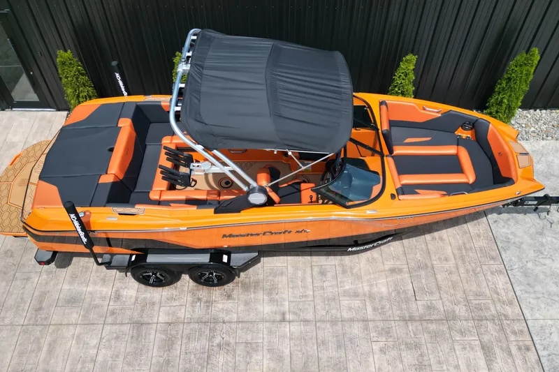 Slide: The Image of 2022 MasterCraft NXT24 boat, orange and black, parked on a trailer, top view. - 16