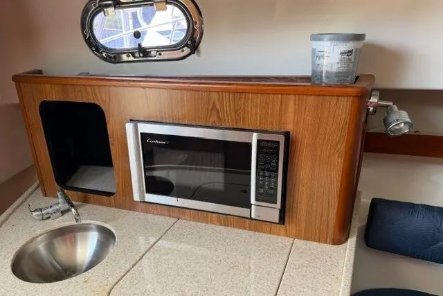 Slide: The Image of 2010 Pursuit OS 285 Offshore boat interior with microwave, sink, and wooden cabinetry. - 66