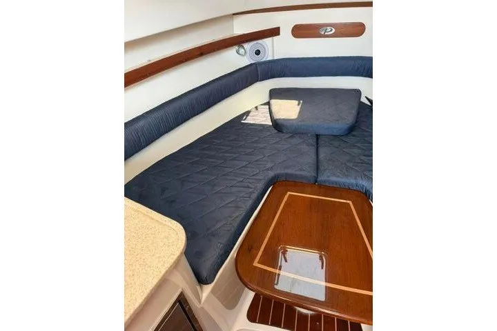 Slide: The Image of 2010 Pursuit OS 285 Offshore cabin interior with cushioned seating and wooden table. - 60