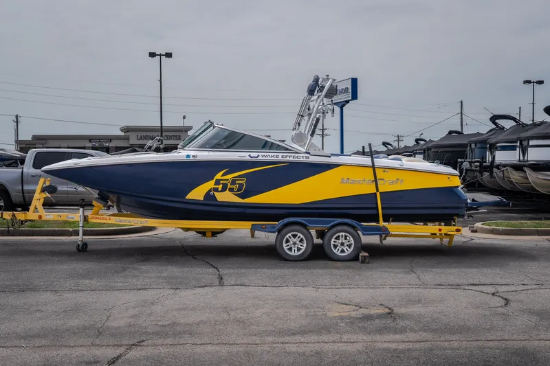 Slide: The Image of 2012 MasterCraft X55 boat on trailer, blue and yellow design, parked outdoors. - 8