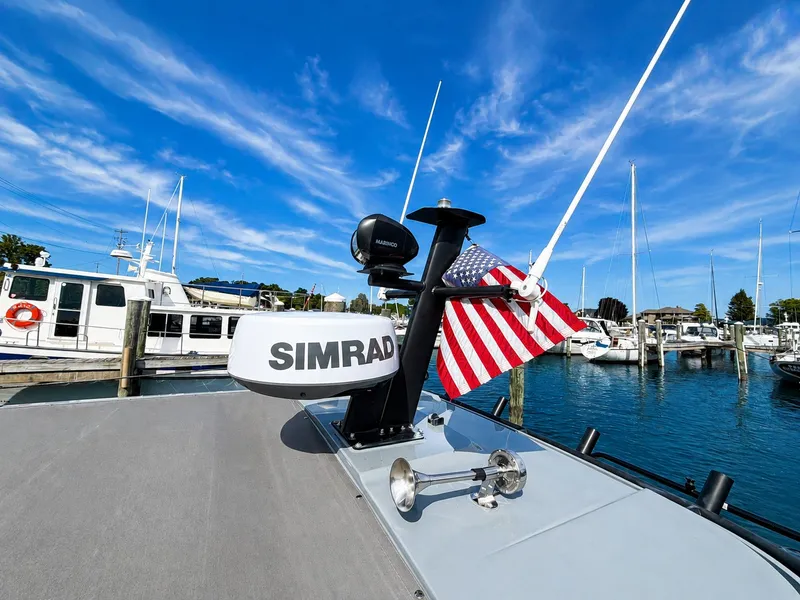Slide: The Image of The image shows the deck of a 2022 Axopar Brabus 37 XC Cross Cabin. There's a Simrad antenna and an American flag. Boats are visible in the harbor background. - 39