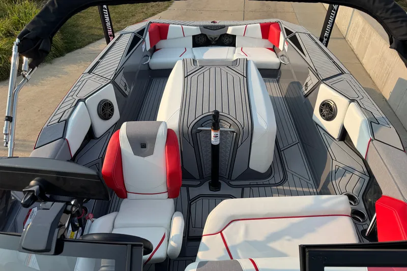 Slide: The Image of 2024 Nautique Ski Nautique boat interior with red and white seating, gray flooring, and speakers. - 22
