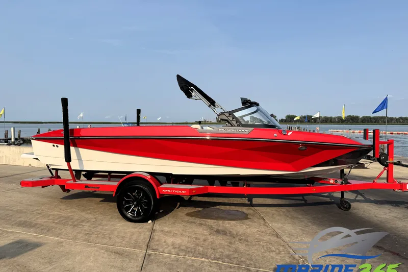 The Image of 2024 Nautique Ski Nautique boat in vibrant red on a matching trailer by the waterfront. - 0