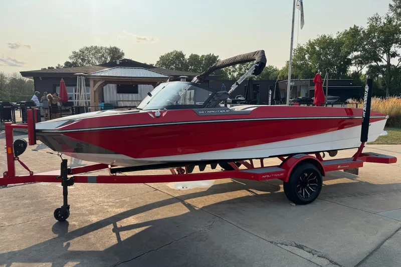 Slide: The Image of 2024 Nautique Ski Nautique boat in red on a trailer, parked outdoors. - 2