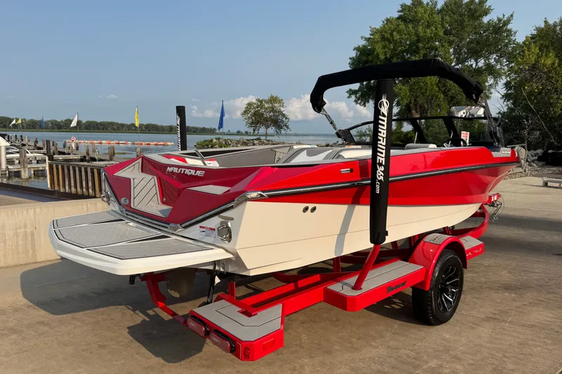 Slide: The Image of 2024 Nautique Ski Nautique boat in vibrant red, docked by a scenic lakeside. - 3