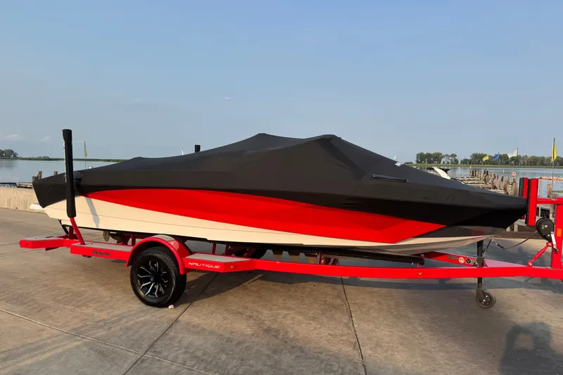 Slide: The Image of 2024 Nautique Ski Nautique boat covered on a red trailer by a lakeside dock. - 36