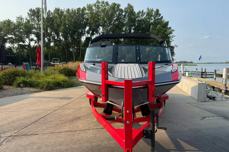 Slide: The Image of 2024 Nautique Ski Nautique boat on red trailer, parked near a lakeside dock. - 4
