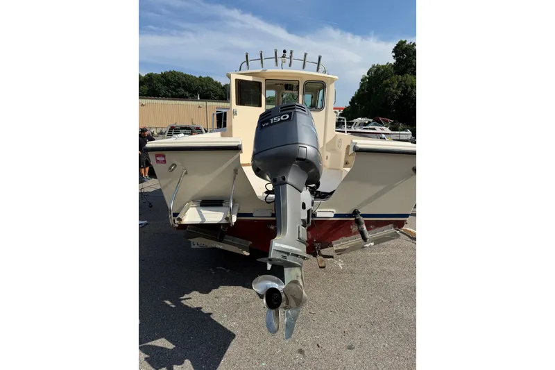 Slide: The Image of 2003 Parker 2120 Sport Cabin boat with outboard motor, parked outdoors on a sunny day. - 16