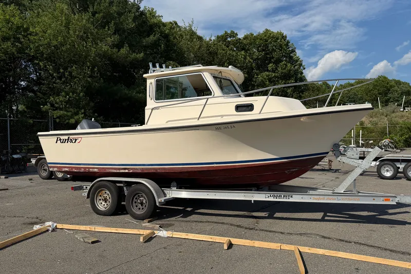 The Image of 2003 Parker 2120 Sport Cabin boat on trailer, parked outdoors with trees in background. - 1