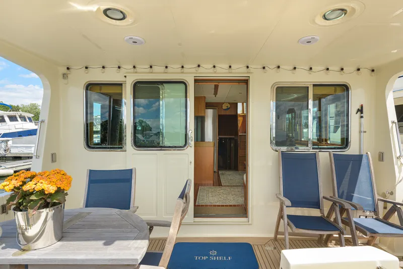 Slide: The Image of Outdoor seating area on a 2017 North Pacific 49 Pilothouse yacht with blue chairs and flowers. - 55