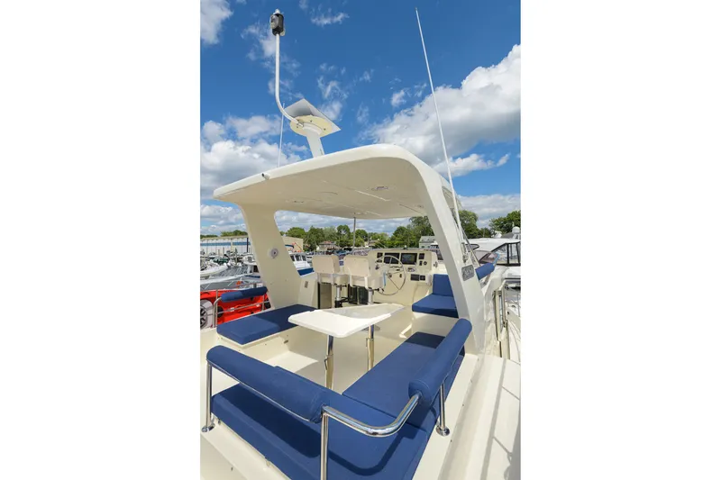 Slide: The Image of 2017 North Pacific 49 Pilothouse yacht with blue seating and helm, under a clear sky. - 61