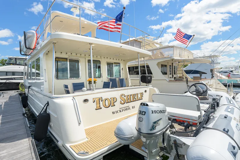Slide: The Image of 2017 North Pacific 49 Pilothouse yacht docked, featuring American flags and a Honda outboard motor. - 48