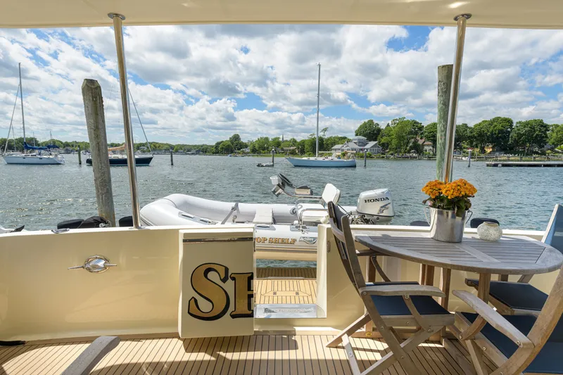 Slide: The Image of Deck view of 2017 North Pacific 49 Pilothouse yacht with table and scenic harbor backdrop. - 52