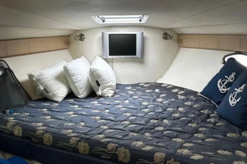 Slide: The Image of 2004 Larson Cabrio 330 cabin interior with cozy bed, pillows, and wall-mounted TV. - 7