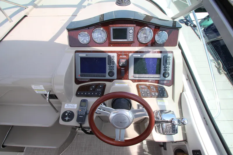 Slide: The Image of 2012 Sea Ray 330 Sundancer helm with dual navigation screens and wood-trimmed steering wheel. - 17