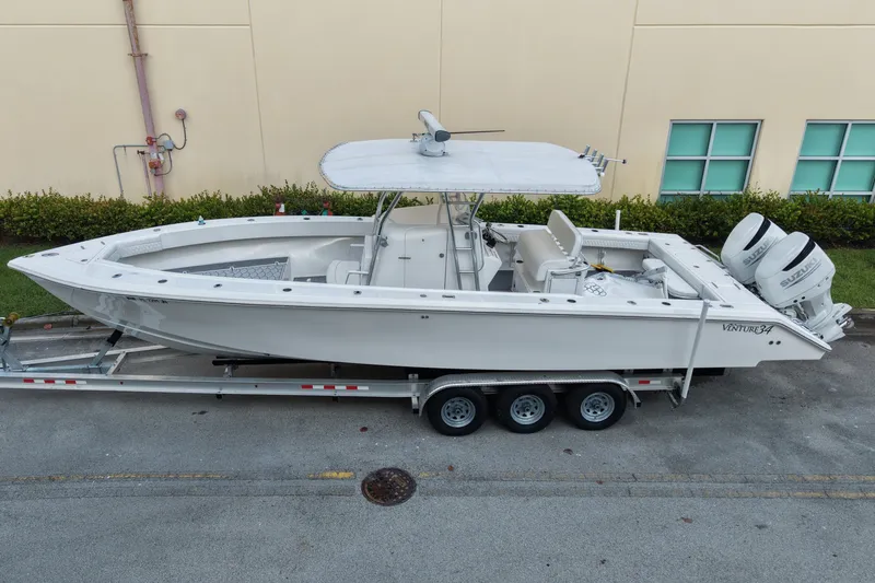 The Image of 1997 Venture 34 Center Console boat on trailer, parked near a beige building. - 0