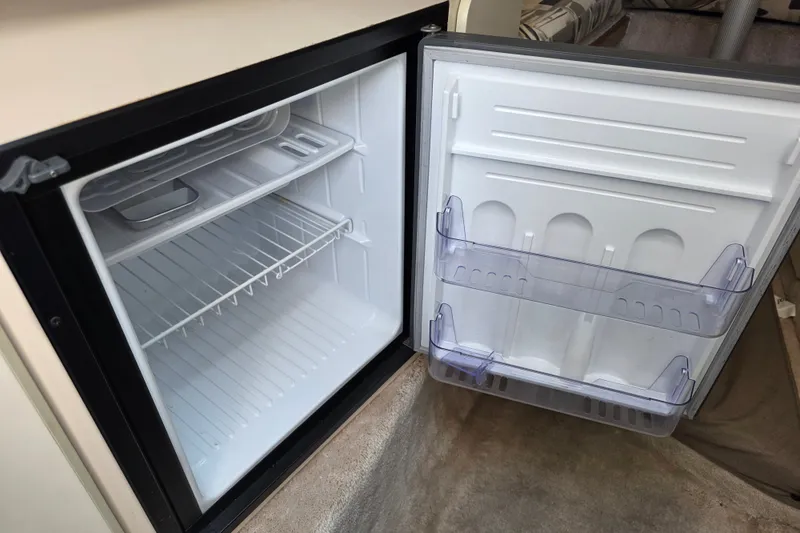Slide: The Image of Open refrigerator inside a 1997 Sea Ray 250 Sundancer boat, showing empty shelves and door compartments. - 20