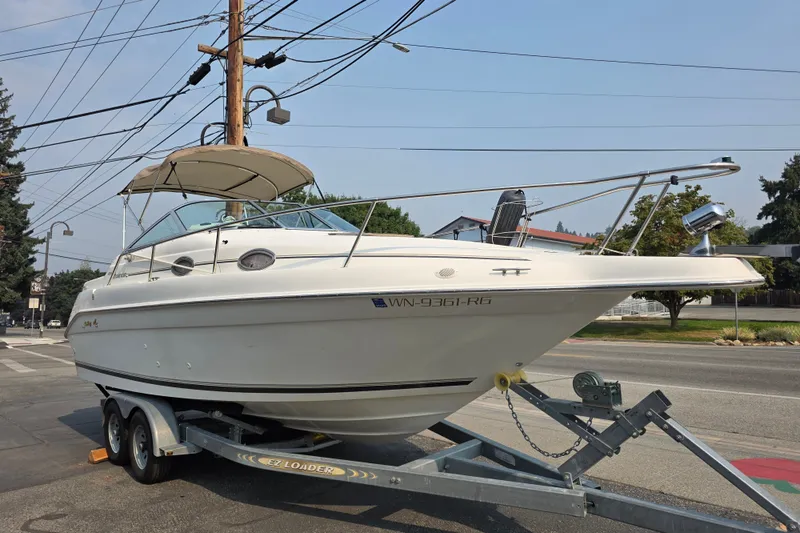 Slide: The Image of 1997 Sea Ray 250 Sundancer boat on trailer, parked on street under clear sky. - 2