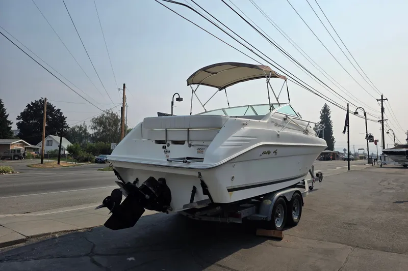 Slide: The Image of 1997 Sea Ray 250 Sundancer boat on trailer, parked near street, under clear sky. - 3