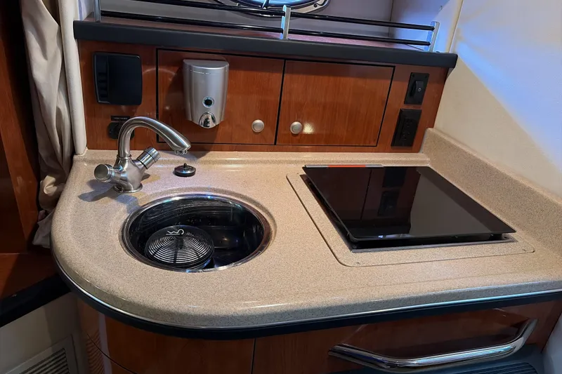 Slide: The Image of 2007 Sea Ray 290 Sundancer galley with sink and stove, featuring wood cabinetry. - 24