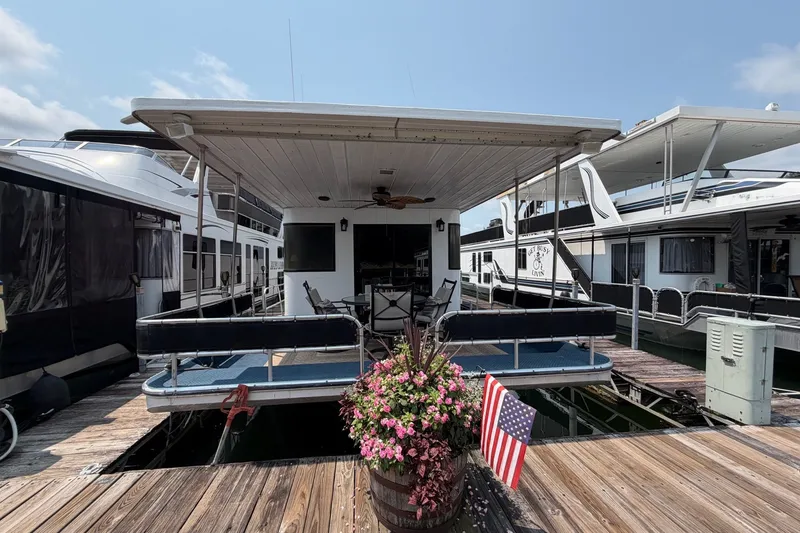 Slide: The Image of Houseboat docked with patio seating, American flag, and flowers; Leisure Time 14x63, 1991 model. - 49