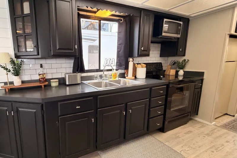 Slide: The Image of Modern kitchen in a 1991 Leisure Time 14x63, featuring black cabinets and stainless steel appliances. - 24