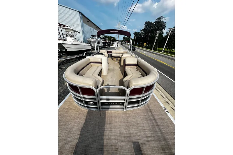 Slide: The Image of 2018 Berkshire Pontoon boat with beige seating, parked near a road under a blue sky. - 4