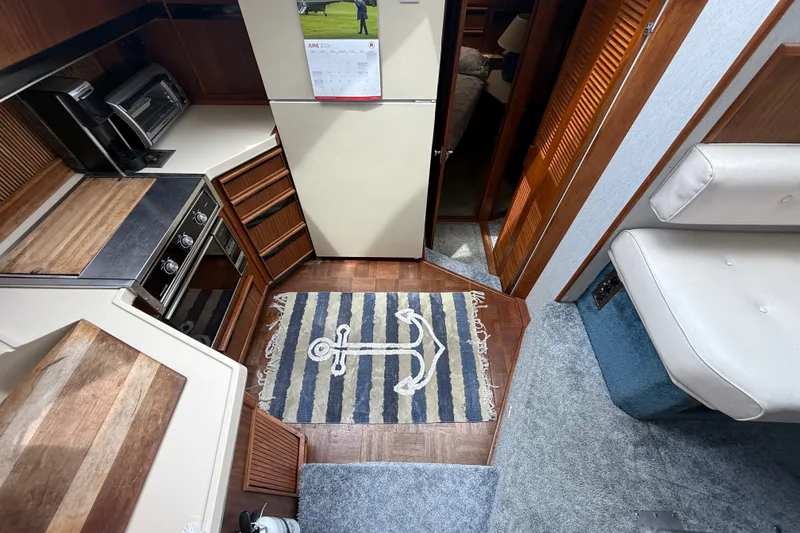 Slide: The Image of 1986 Sea Ray 410 Aft Cabin interior with kitchen, anchor rug, and seating area. - 24