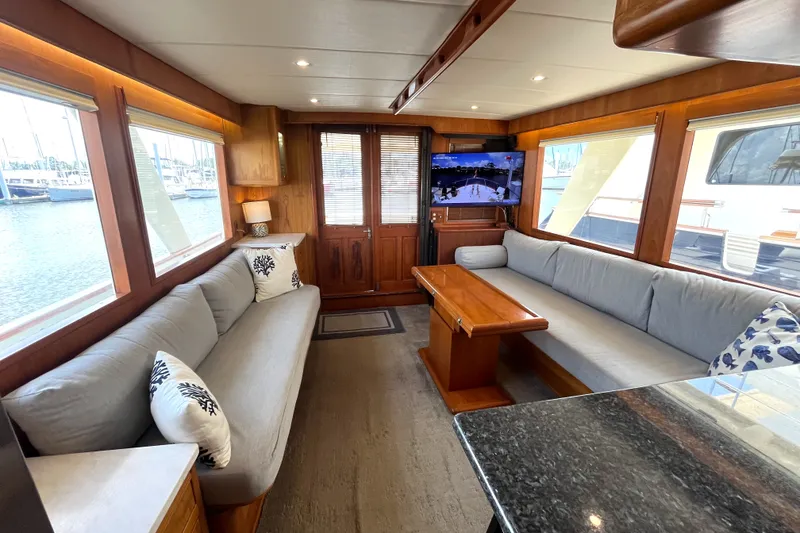 Slide: The Image of The 2002 Grand Alaskan 53 RPH salon features cozy sofas, a wooden table, and windows with marina views. - 7