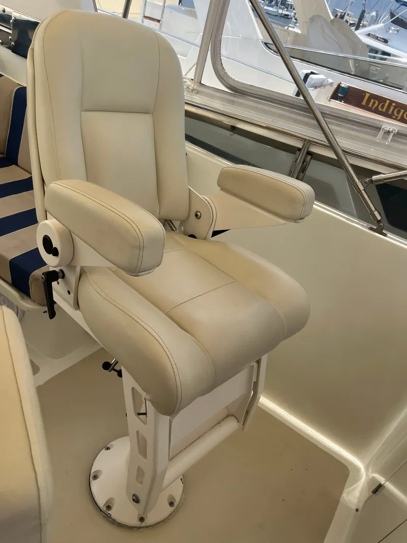 Slide: The Image of A beige captain's chair with armrests on a boat, surrounded by other seats and windows. - 44