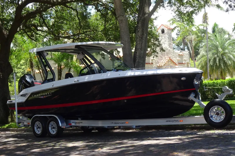 The Image of 2025 Monterey Elite 27 OB boat on trailer, parked under trees, showcasing sleek design. - 0