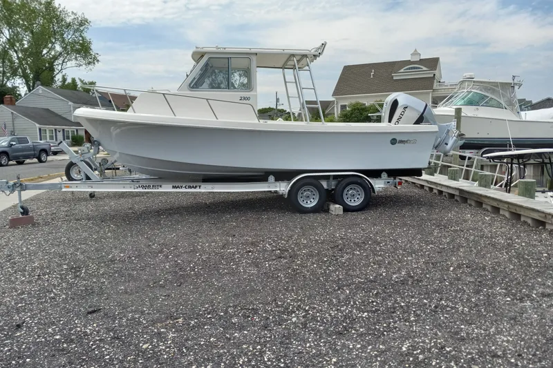 Slide: The Image of 2022 May-Craft 2300 Pilot House boat on trailer, parked near waterfront homes. - 0