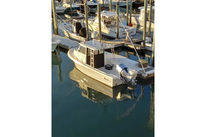 The Image of 2022 May-Craft 2300 Pilot House boat docked in a marina, reflecting on calm water. - 4