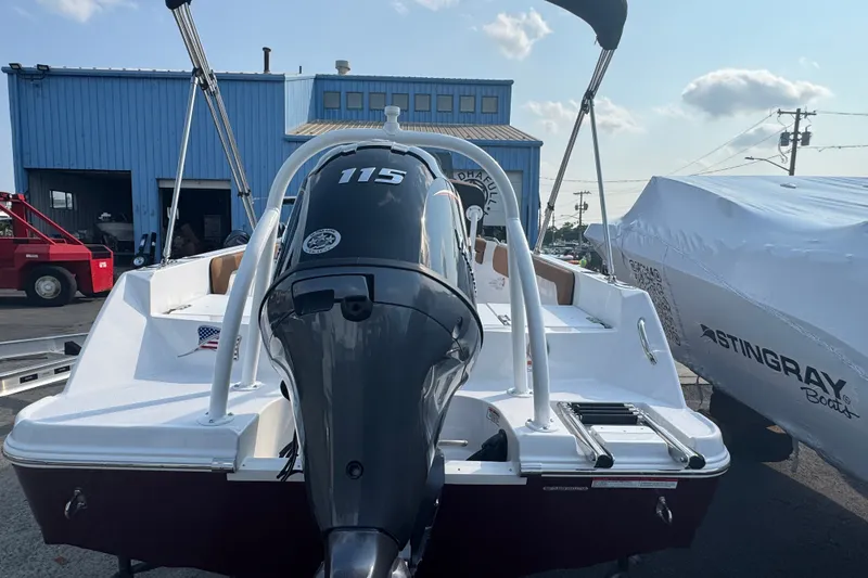 Slide: The Image of 2027 Stingray 17 CC boat with 115 HP engine, parked outdoors near a blue building. - 2