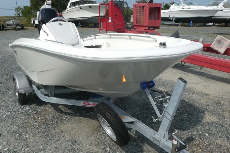 Slide: The Image of 2027 Boston Whaler 130 Super Sport boat on trailer, parked in a marina. - 2