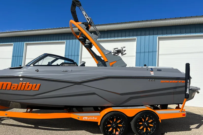 Slide: The Image of 2023 Malibu Wakesetter 22 LSV boat in gray and orange, parked outside a blue building. - 6
