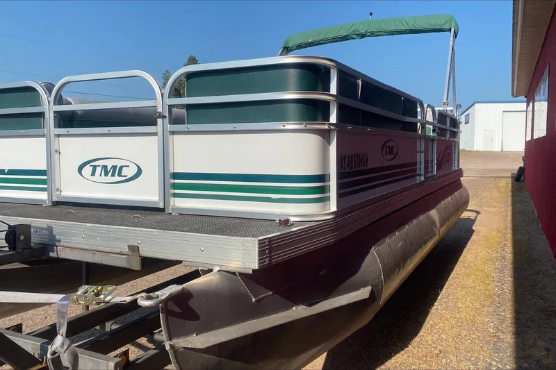 Slide: The Image of 2007 TMC 2200LE pontoon boat with green accents, parked on a trailer. - 6