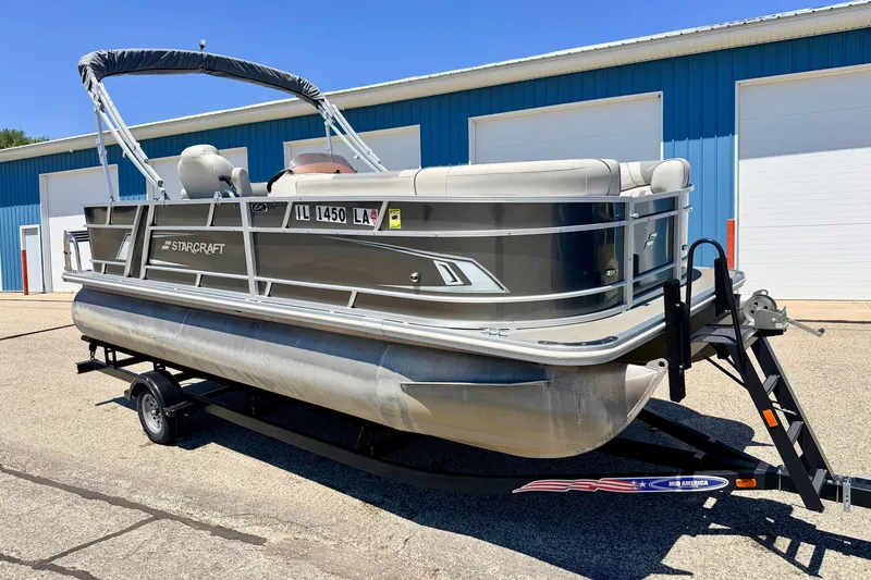Slide: The Image of 2021 Starcraft EX 20 C pontoon boat on trailer, parked near blue building. - 5
