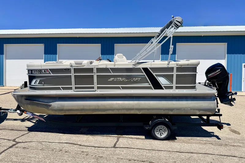 Slide: The Image of 2021 Starcraft EX 20 C pontoon boat on trailer, parked outside blue building. - 6