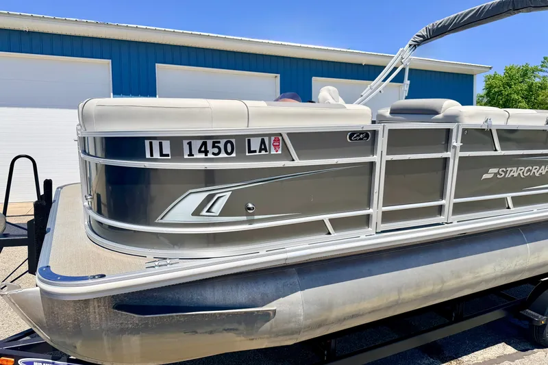 Slide: The Image of 2021 Starcraft EX 20 C pontoon boat on trailer, parked outside a blue building. - 14
