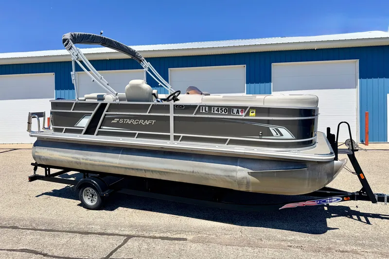 The Image of 2021 Starcraft EX 20 C pontoon boat on trailer, parked outside blue building. - 1