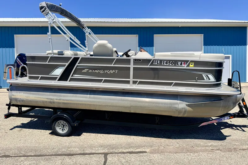 Slide: The Image of 2021 Starcraft EX 20 C pontoon boat on trailer, parked outside blue building. - 3