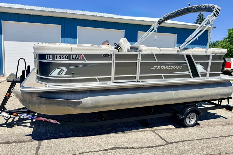 Slide: The Image of 2021 Starcraft EX 20 C pontoon boat on trailer, parked outside blue building. - 4
