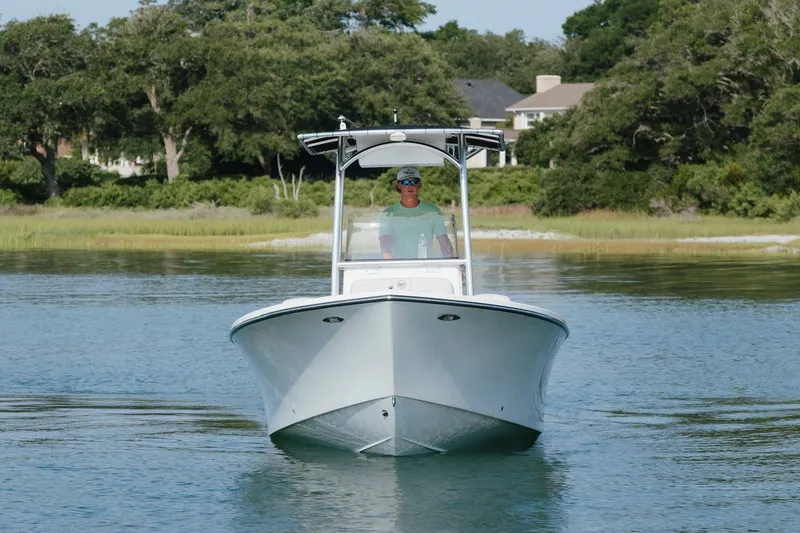 Slide: The Image of 2023 May-Craft 2300 CCX boat cruising on a calm lake with lush greenery. - 1