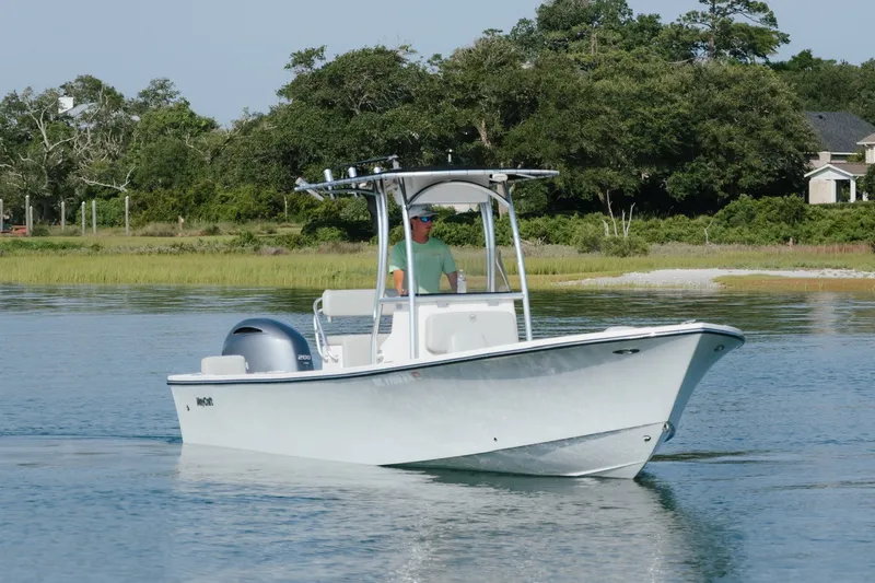 Slide: The Image of 2023 May-Craft 2300 CCX boat cruising on calm water near a lush shoreline. - 4