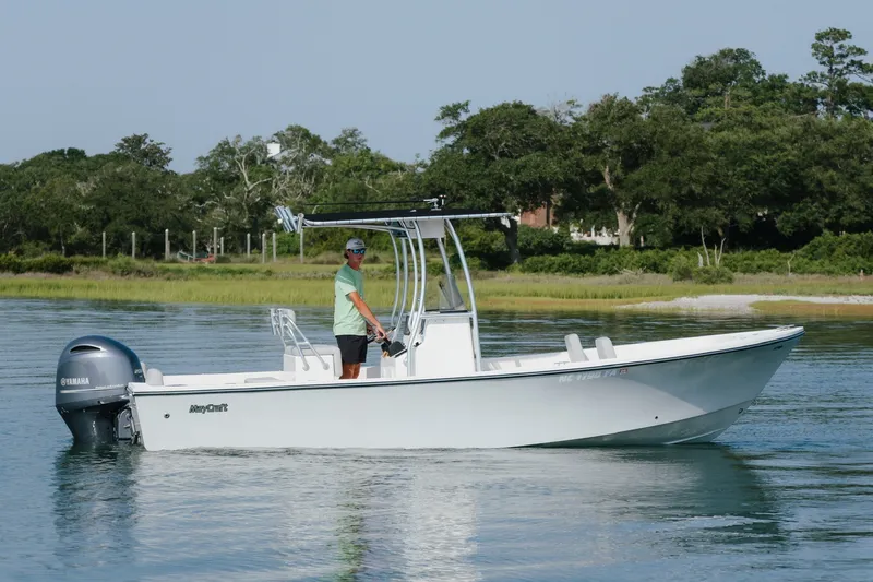 Slide: The Image of 2023 May-Craft 2300 CCX boat cruising on calm water with lush greenery in the background. - 2