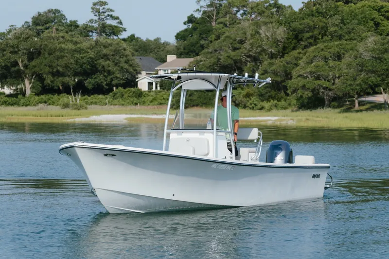 Slide: The Image of 2023 May-Craft 2300 CCX boat cruising on a calm lake with lush greenery. - 3