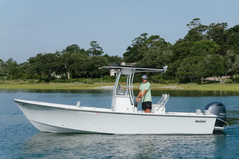 Slide: The Image of 2023 May-Craft 2300 CCX boat cruising on calm water near a lush shoreline. - 14